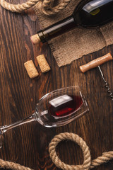Glass with wine, bottle, corkscrew and burlap, top view