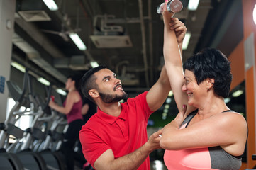 Middle aged woman working out with coach in gym
