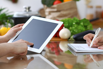 Close-up of  human hands are gesticulate over a tablet in the kitchen. Friends having fun while choosing menu or making online shopping