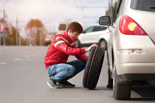 Young upset man changing tyre wheel on cityroad