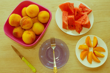 Slices of watermelon and peaches on a plate on the wooden table.