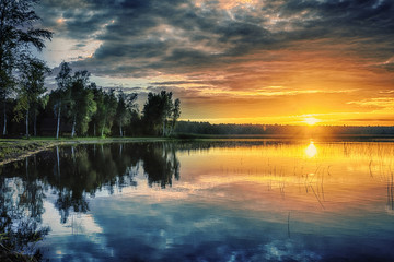 Obraz premium Beautiful red sunset landscape on lake with trees and blue clouds
