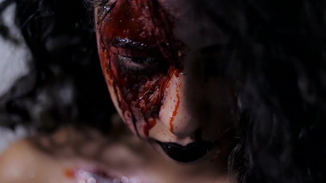 Scary portrait of young girl with Halloween blood makeup. Beautiful latin woman with curly hair looking into camera in studio. Living dead greasepaint. Slow motion.