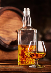 Glass and bottle of Cognac on wodden table old oak barrel defocussed