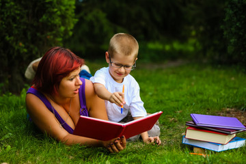 Picture of beautiful woman with son sitting down on green grass field and read fairytale in park