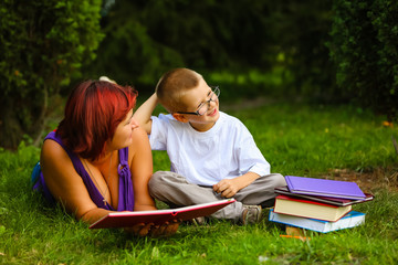 Picture of beautiful woman with son sitting down on green grass field and read fairytale in park