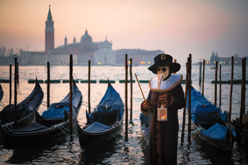 Fototapeta na wymiar Man in Carnival costume with gondolas on Grand Canal against San Giorgio Maggiore church