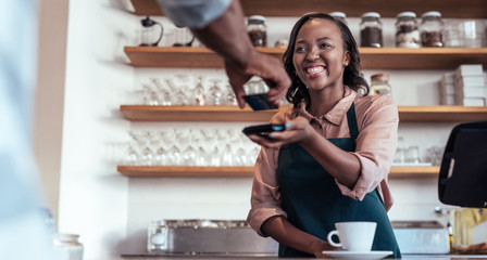 Smiling barista using nfc technology for payment from a customer