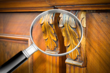 Detail of an antique wooden italian furniture just restored with a magnifying glass on foreground...