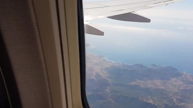 View through a passenger airplane window flying over south-east coast of Crimea. Aerial view of mountains and the Black Sea on a sunny day. Aircraft flight from Simferopol to Krasnodar.