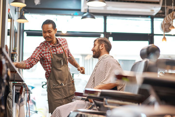 Positive thai hairdresser going to do a haircut for a bearded man