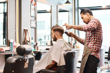 Concentrated professional barber makgng a haircut for a bearded man