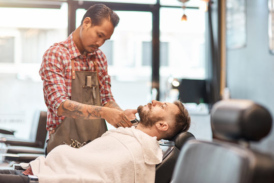Professional barber cutting a beard of a handsome man