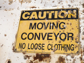 dirty, old yellow and black Caution - Moving Conveyor No Loose Clothing sign