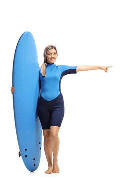 Woman in a wetsuit holding a surfboard and pointing