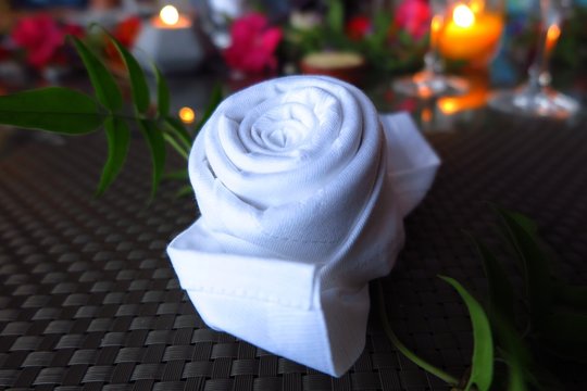 white napkin folded into shape of rose on candlelit table with flowers