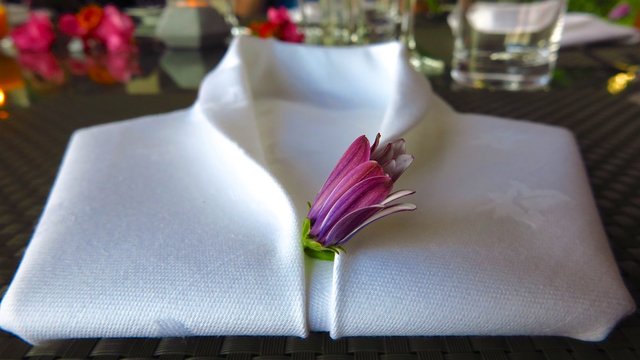 White napkin folded into shape of tuxedo shirt with flower
