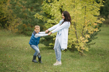 Fototapeta premium young mother and her son play in the autumn in the park, they are warmly dressed