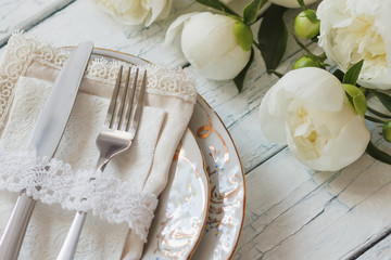 Tableware and silverware with a bouquet of white peonies on the white wooden boards