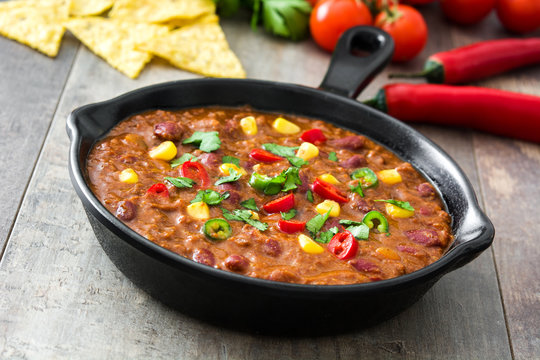 Traditional mexican tex mex chili con carne in a frying pan on wooden table