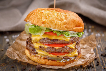 Big hamburger with three beef cutlet and vegetables on wood background.