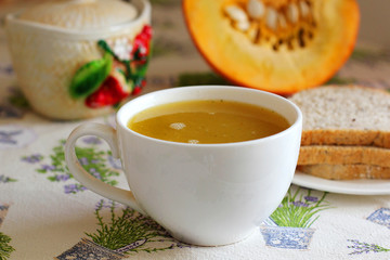 Pumpkin soup in white mug on table.