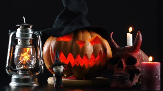 Halloween. Pumpkin, skull, oil lamp, candle, witch standing on table.