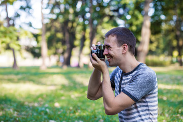 Young man taking pictures on retro camera in city park