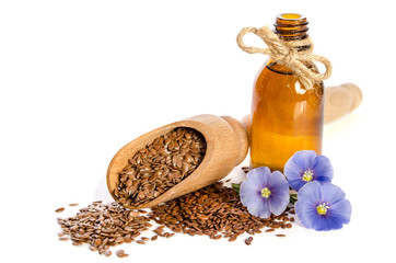 Flax seeds in the wooden scoop, bottle with oil and  beauty flowers isolated on white background.