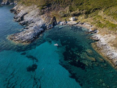 Vista aerea di una barca ormeggiata che galleggia su un mare trasparente. Piccola casa sulla costa rocciosa del Cap Corse. Vacanze estive. Coste della Corsica, spiagge e rocce
