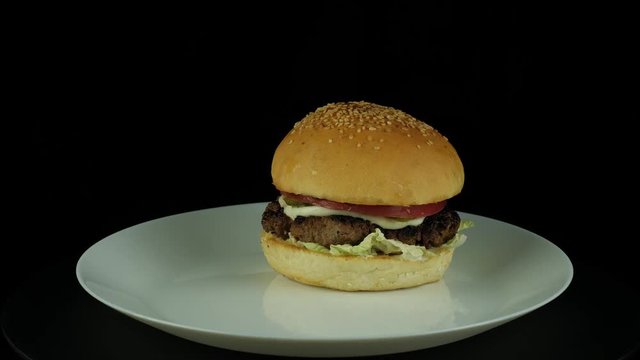Burger with cheese grilled beef Patty, pickles, tomatoes and lettuce, roating in plate on a black background, 360 degree, 4k uhd,shoot for restaurant menu