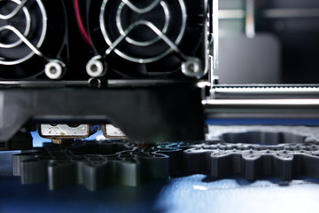 FDM 3D-printer manufacturing spur gears from silver-gray filament on blue print tape- close up on nozzle and hotend - background and foreground blanked out blurry