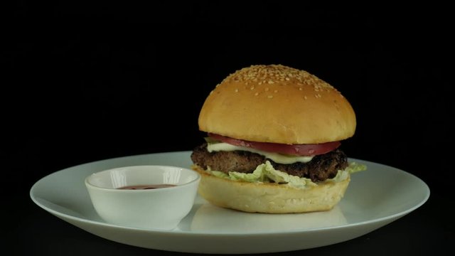 Burger with cheese grilled beef Patty, pickles, tomatoes and lettuce, roating in plate on a black background, 360 degree, 4k uhd,shoot for restaurant menu