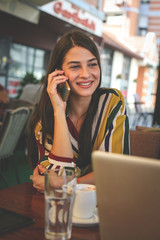 Young woman having coffee break and talking on smart phone in cafe.