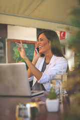 Young smiling business woman working in cafe and talking on smart phone.  Girl appears to someone in the passage.