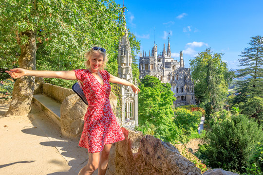 Happy blonde caucasian woman with open arms in Sintra, Portugal. Female tourist enjoying in a sunny day. Aerial view of Regaleira Palace.