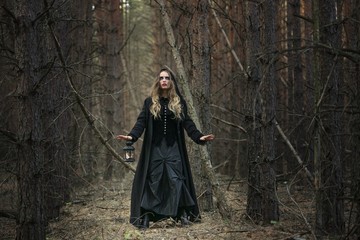 Halloween. beautiful girl with a lantern in a black dress in the forest.