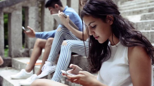 Teenagers with smartphones and tablets on stone steps.