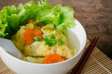 Close up minced pork and shrimp wonton soup in white bowl on wood table. Homemade delicious wonton in clear soup for breakfast or lunch or dinner. Wonton or dumpling soup is popular Chinese food.