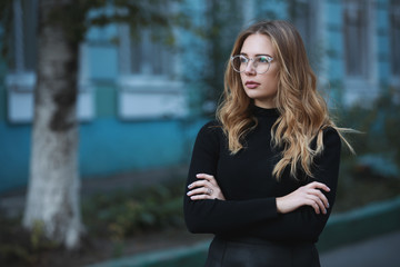 Fototapeta premium Portrait of young woman student against blue university building background, arms crossed