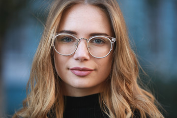 Myopia, close-up portrait of young woman student in eyeglasses for good vision look at camera, blue building background