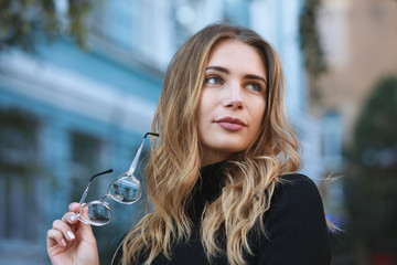 Myopia, portrait of young woman student holding eyeglasses for good vision, blue building background