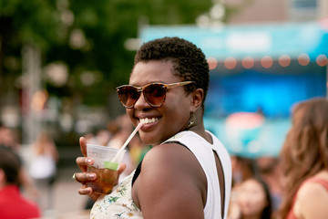 Attractive african american girl drinking from a plastic glass in the crowd of a summer music festival