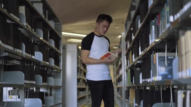 Focused student picking a book from the shelf and start reading in library in college. Slow motion