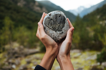 a girl holding a rock with a heart at the mountains background