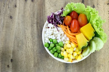 healthy and diet food , fresh vegetable salad (lettuce, tomato, pumpkin, carrot, corn, millet, cucumber, purple  cabbage and peanuts) in white bowl on wood table background have copy space