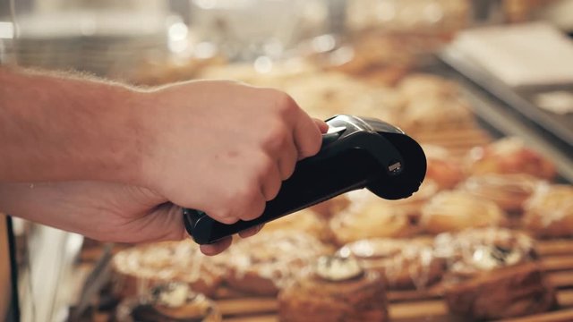 Close-up of woman making payment through NFC in bakery, cafe restaurant, mobile phone contactless pay for bill with terminal, banking