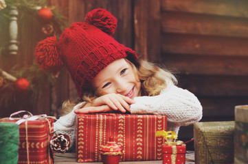 Obraz na płótnie Canvas happy child girl in red hat and scarf wrapping Christmas gifts at cozy country house, decorated for New Year and Christmas. Preparations for holidays with kids.