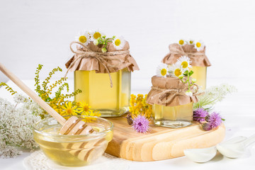 Natural light liquid honey. Honey in glass jars and dipper on white background with flowers.