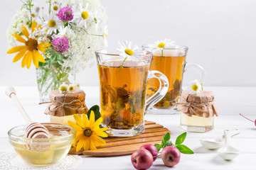 Herbal tea with herbs and flowers in a glass tea pot with honey. Bouquet of flowers on white table